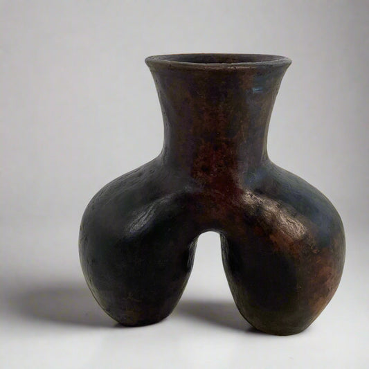 Black ceramic vase on a textured surface with a white curtain background