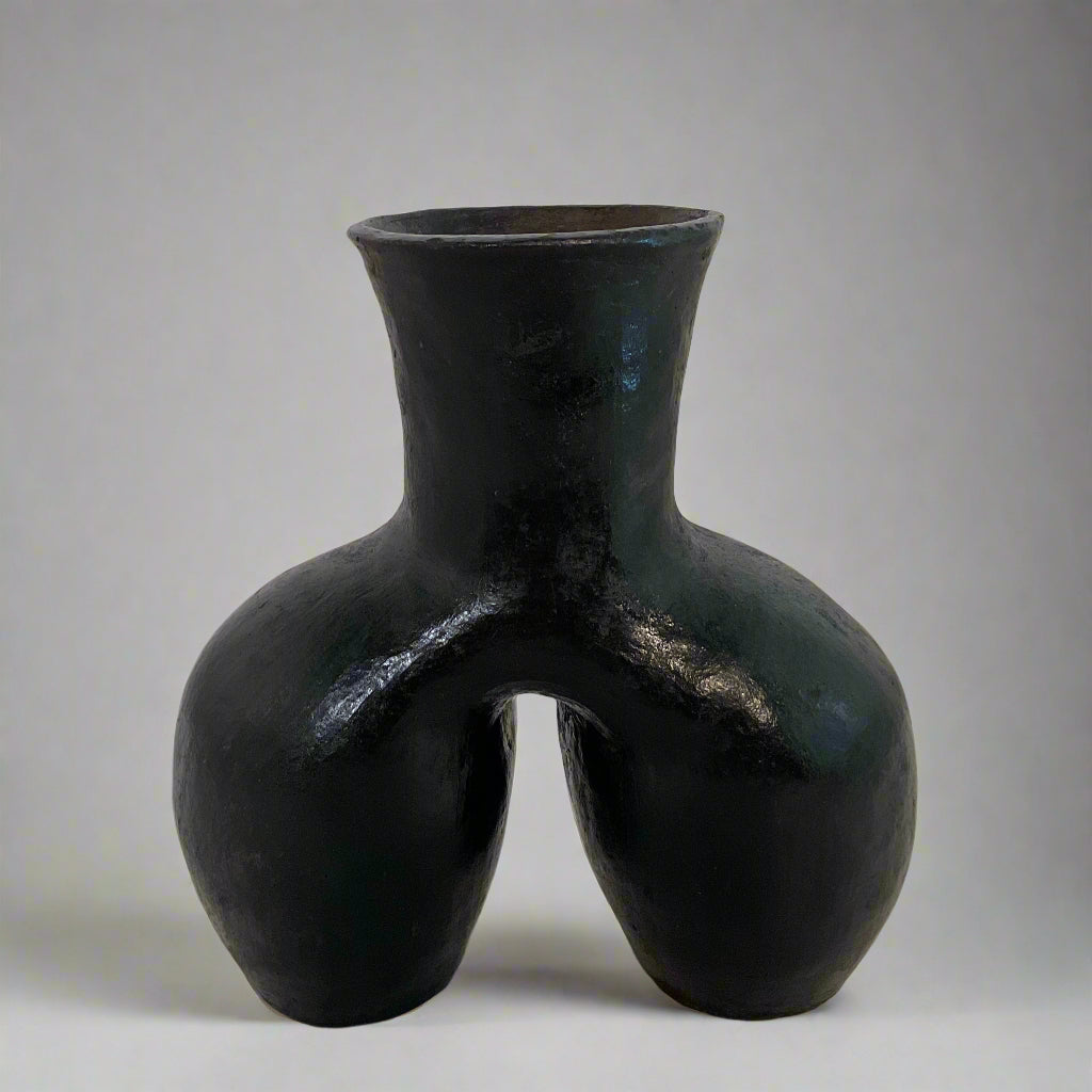 Black vase with a unique design on a textured surface with a light curtain background