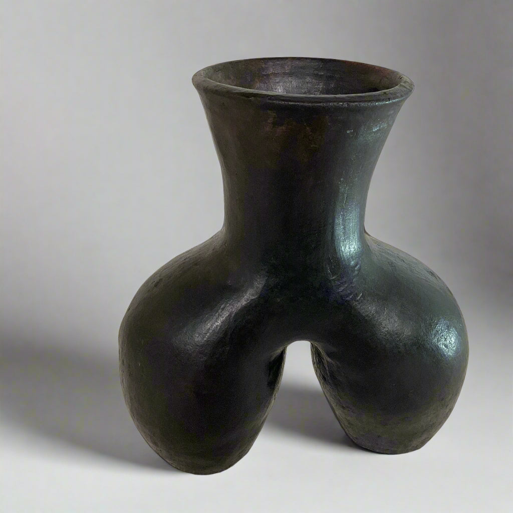 Black ceramic vase with unique design on a textured surface