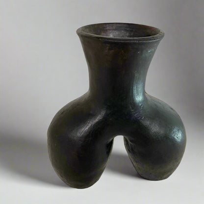 Black ceramic vase with unique design on a textured surface