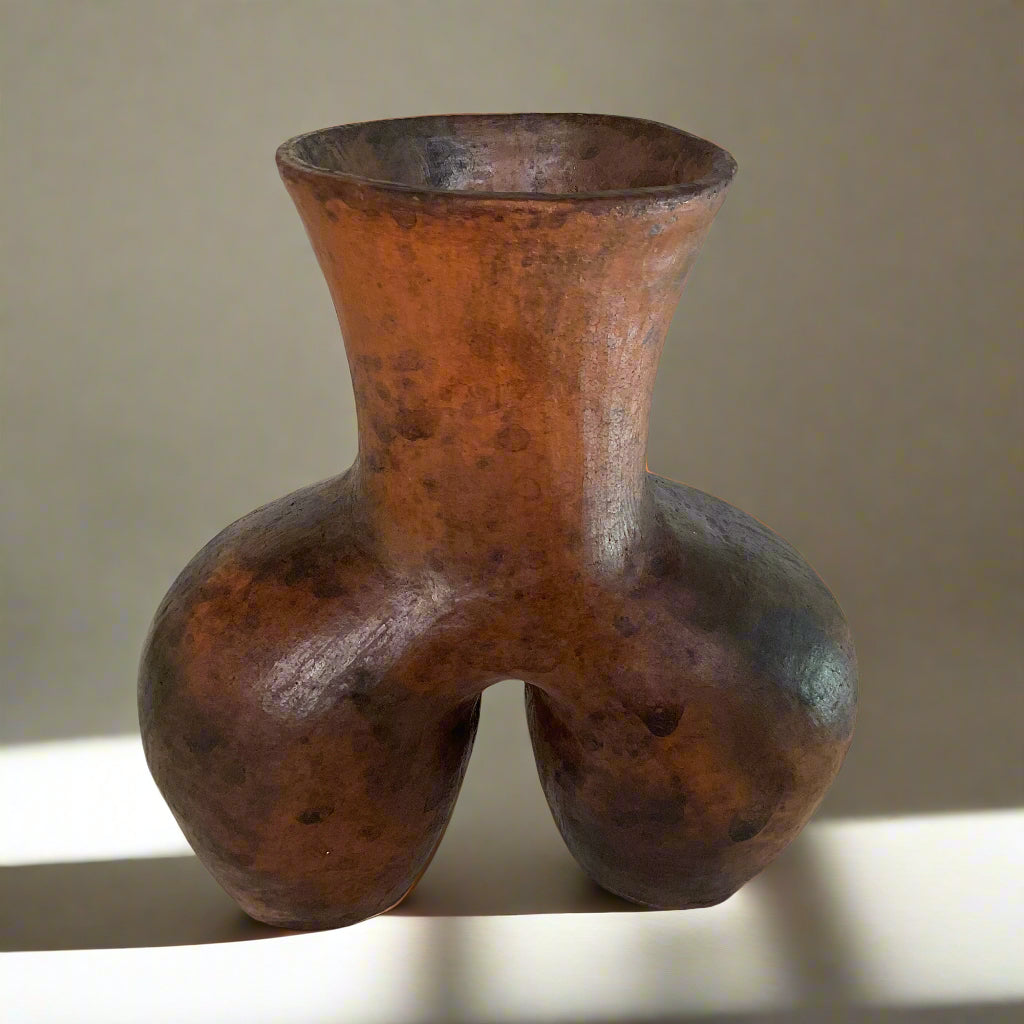Brown ceramic vase on a textured surface with a white curtain background