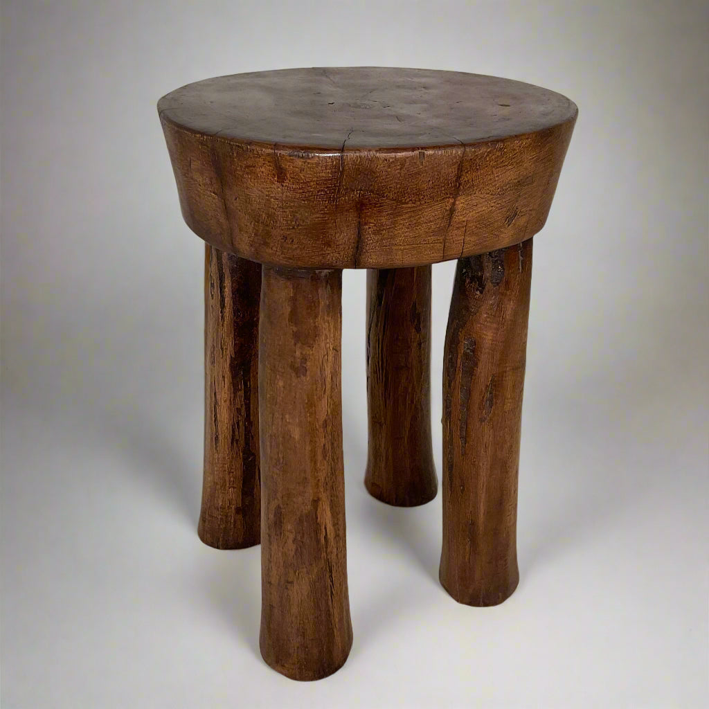 Wooden stool with four legs on a textured surface and white curtain background