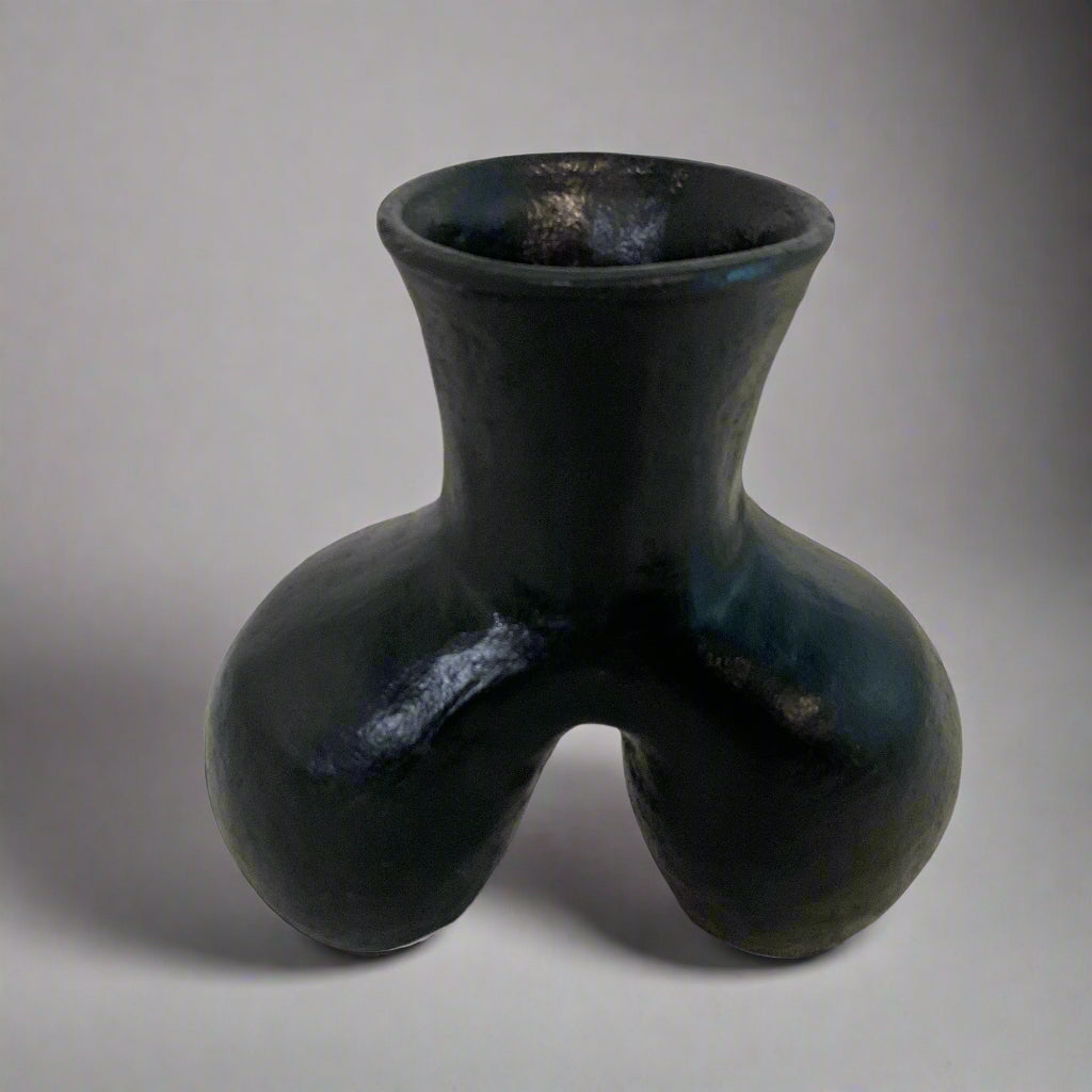 Black ceramic vase on a textured surface with a light curtain background