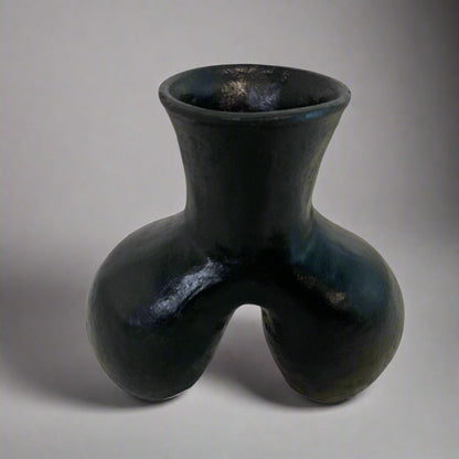 Black ceramic vase on a textured surface with a light curtain background