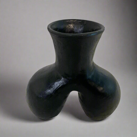 Black ceramic vase on a textured surface with a light curtain background