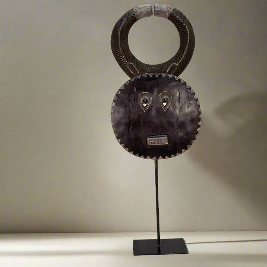 Decorative metal mask on a stand against a white curtain background