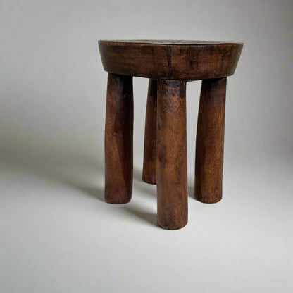 Wooden stool with three legs on a textured surface with a white curtain background