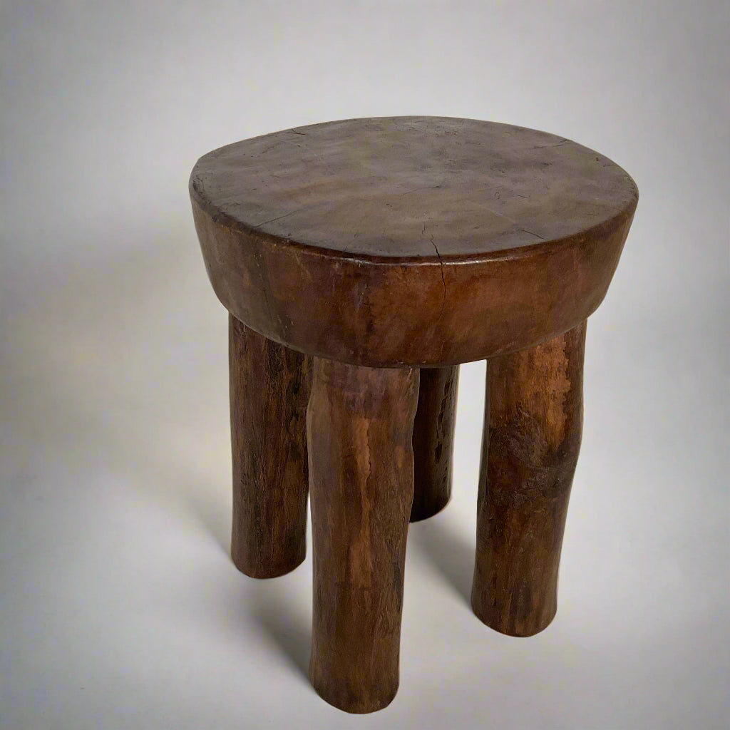 Wooden stool with a round top and four thick legs on a textured surface.